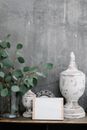 Board with blank paper sheet placed near shabby retro decorations and plant twigs against gray wall