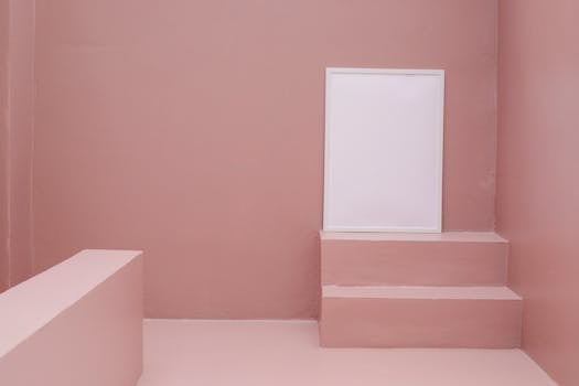 Clean minimalist room with a blank white poster frame on stairs against a soft pink wall.