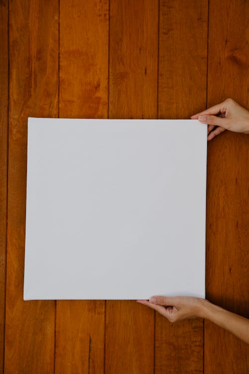 Free Top view crop anonymous female showing square blank canvas placed on wooden surface Stock Photo