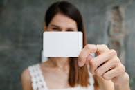 Young blurred female showing white blank business card and looking at camera in light room