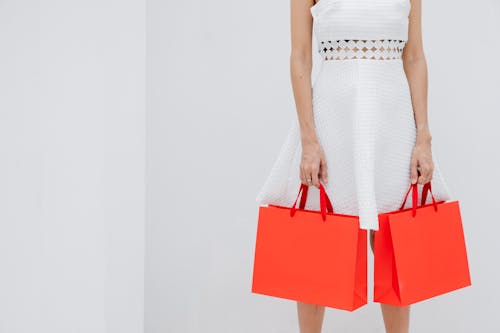 Crop unrecognizable woman carrying red shopping bags in studio