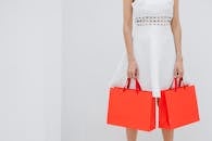 Crop unrecognizable woman carrying red shopping bags in studio