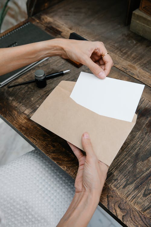 Free Crop unrecognizable woman placing blank paper in envelope Stock Photo