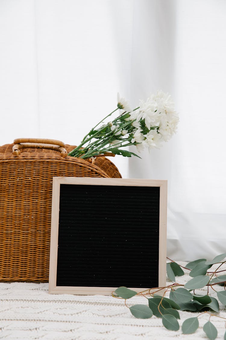 Letter Board Placed Near Wicker Bag And Blooming Flowers