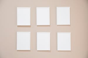 Rows of blank white rectangular frames hanging on light pink wall in studio