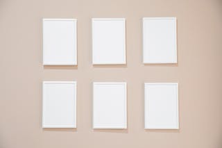 Rows of blank white rectangular frames hanging on light pink wall in studio