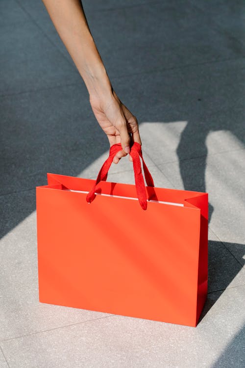 High angle of crop anonymous female buyer taking red paper bag with purchase in sunshine