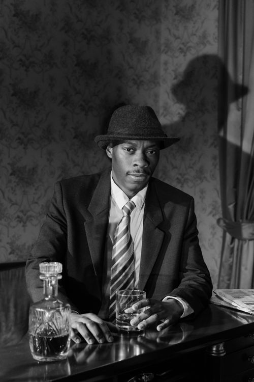 Free Black and white portrait of a noir detective character with whiskey, evoking 1950s detective fiction. Stock Photo