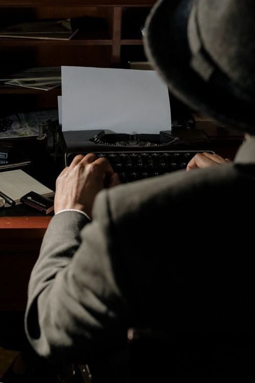 Free Cinematic scene of a detective typing on a vintage typewriter in dim light. Stock Photo