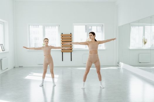 Two women practicing dance poses in a bright, minimalist studio with mirror reflections.