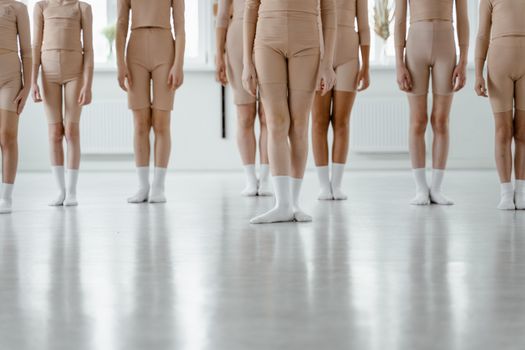 Dancers standing in a minimalist setting wearing beige outfits and white socks.