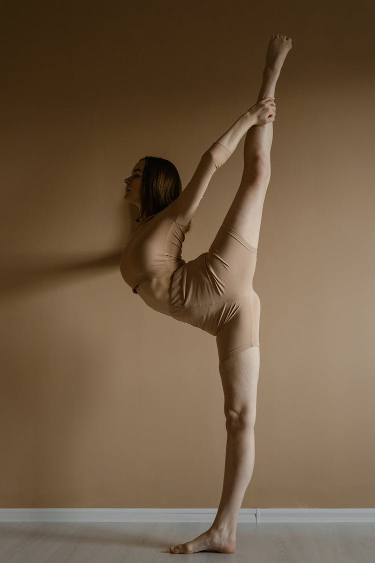 Side View Of A Flexible Woman In Beige Leotard Raising Her Leg