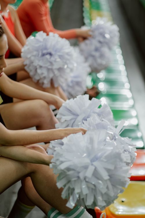 Free A group of cheerleaders holding pom poms while sitting on colorful stadium bleachers. Stock Photo
