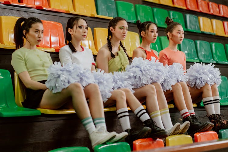 Cheerleaders Sitting On Bleachers While Holding Pom-poms