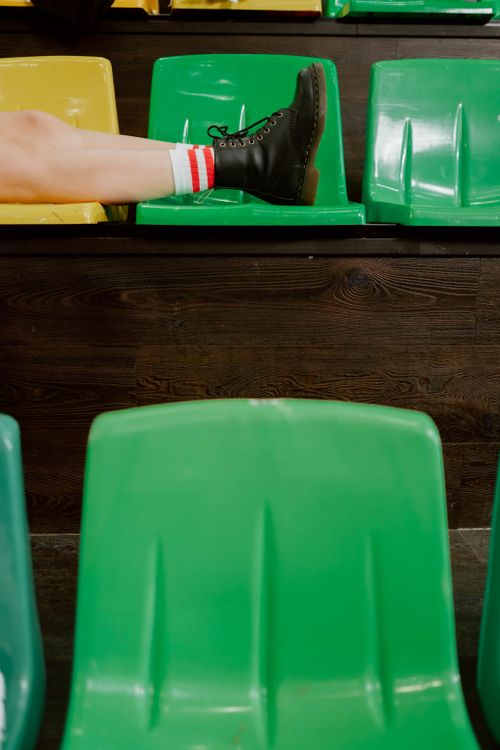 Free Person lounging in bleachers wearing boots and striped socks, emphasizing relaxation. Stock Photo