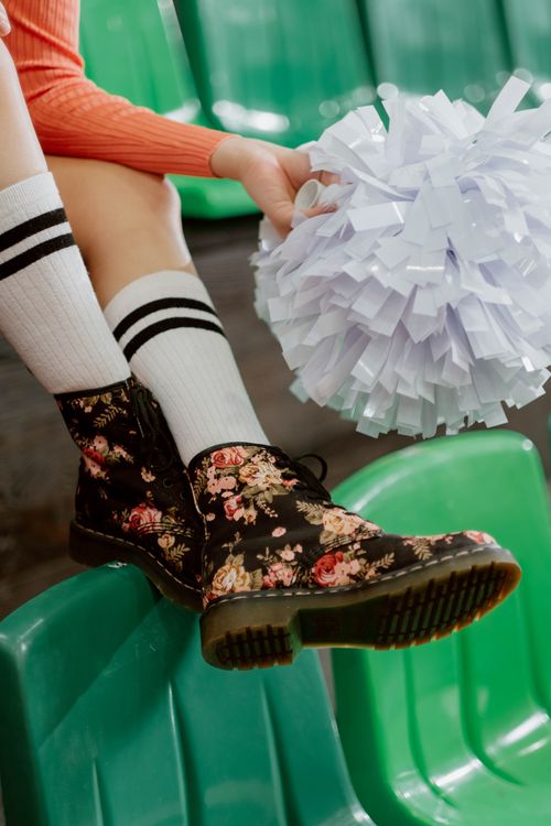 Free Floral boots and a cheer pom pom on green seats reflecting a sporty fashion vibe. Stock Photo