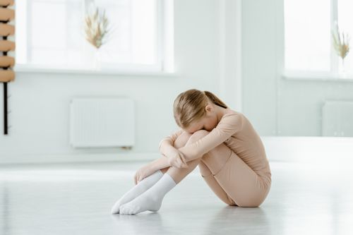 Free A young girl in neutral attire sits on the floor, head down, in a bright minimalist space. Stock Photo