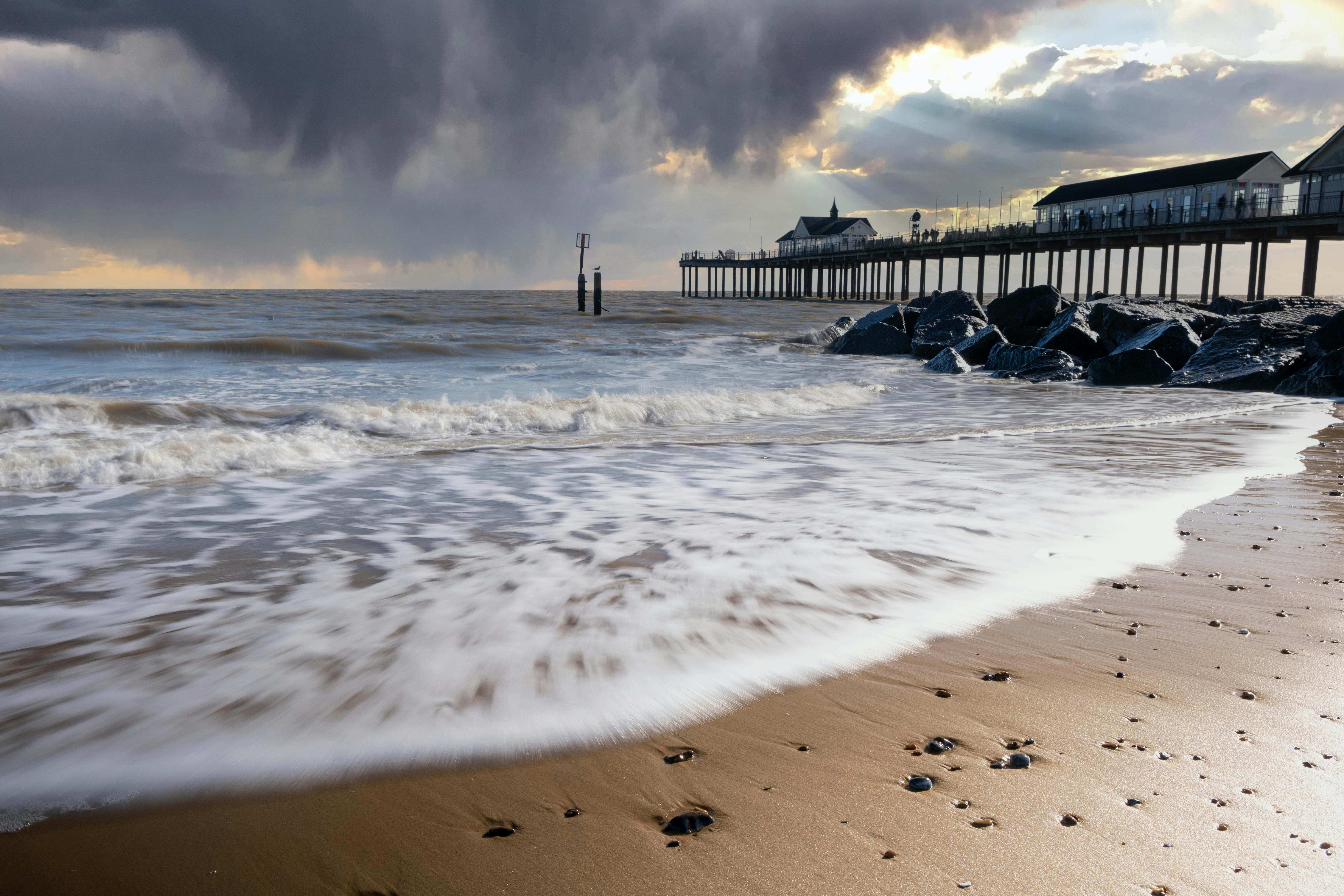 A stunning view of Southwold Pier with dramatic clouds and gentle waves on a sandy beach.