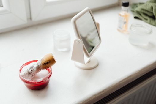 Shaving brush and mirror on a bathroom windowsill, perfect for skincare routines.