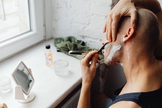 A bald man using shaving foam and a razor, seen in a bathroom setting.