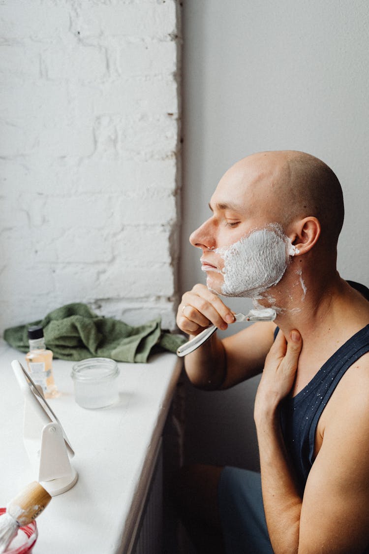 Man Shaving In Front Of A Small Mirror Standing On A Windowsill 