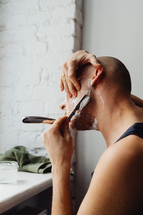 Free A bald man uses a straight razor and shaving cream in a well-lit room. Stock Photo