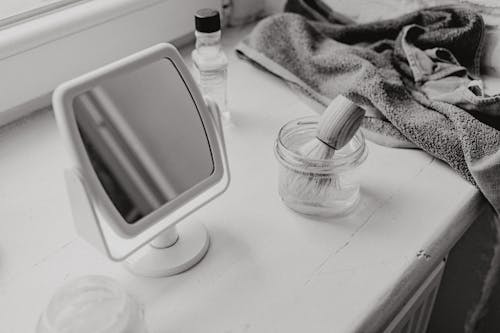 Grayscale Photo of a Mirror and a Brush in a Container