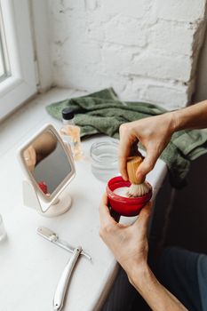 Hands preparing shaving cream with brush in a classic grooming setup.