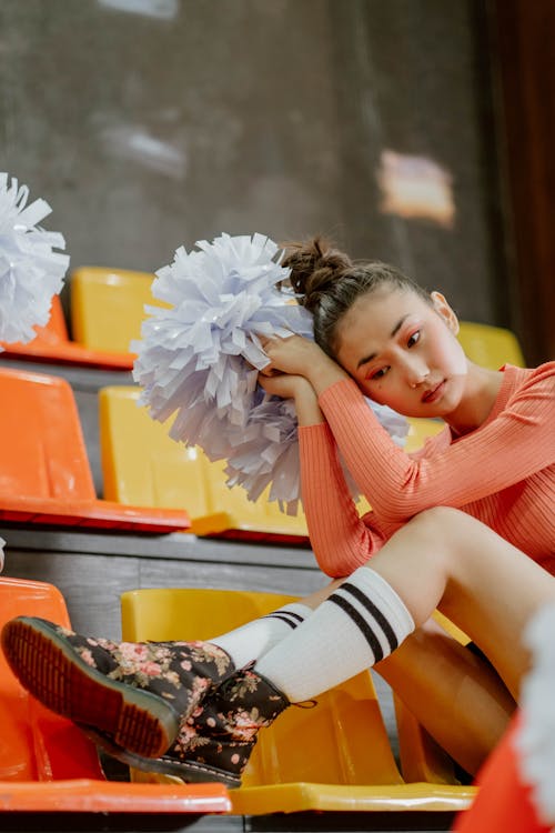 A Woman Sitting on the Bleachers Holding Pompoms