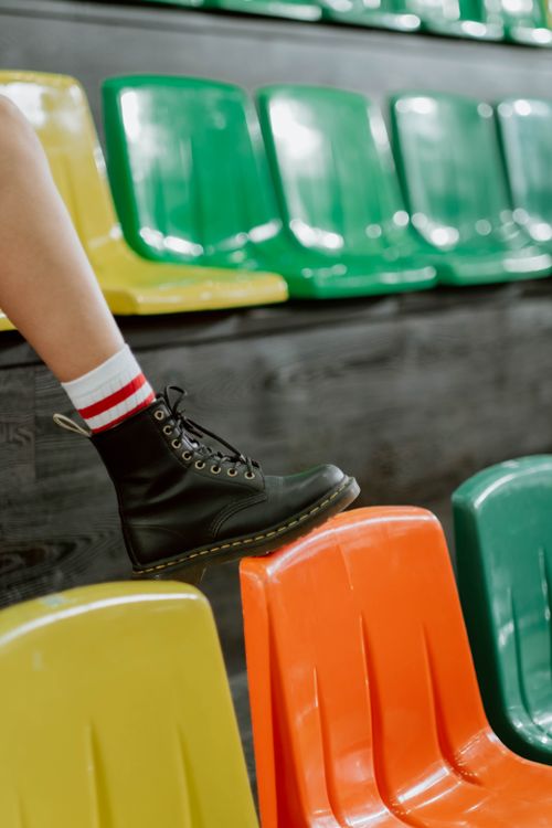 Free Leg in black boot with colorful seats in background. Urban style and footwear focus. Stock Photo