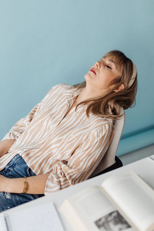 Free A woman in a striped blouse relaxes on a chair in an indoor setting with books. Ideal for lifestyle imagery. Stock Photo