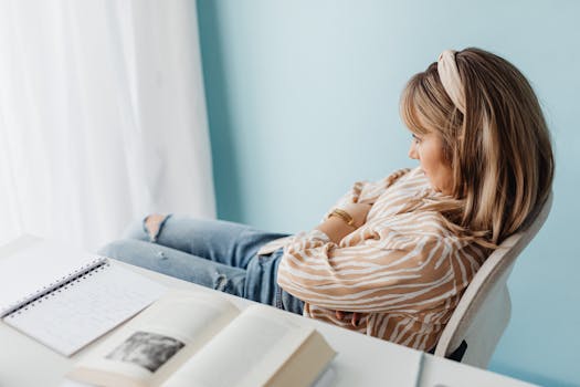 Side view of a woman sitting with arms crossed in a bright office with books on the table.