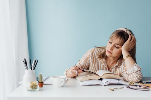 Free Woman sitting at a desk, reading with a pen in her hand and looking thoughtful. Stock Photo