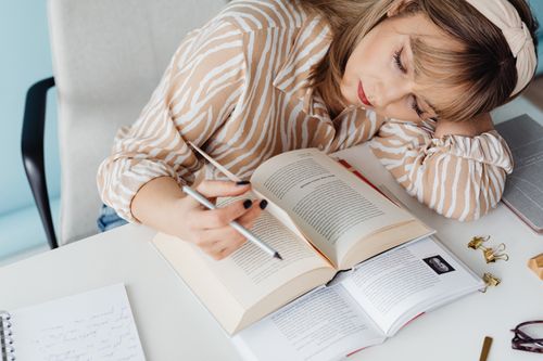 Free A woman in a striped shirt rests while studying at a desk with open books. Stock Photo