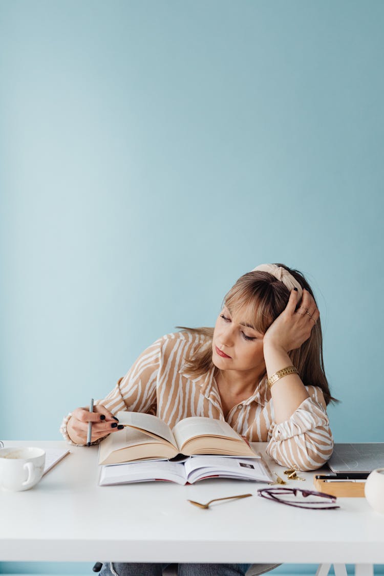 A Woman Resting Her Head On Her Hand While Reading A Book