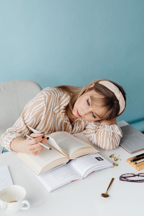 Free Caucasian woman with a headband lost in thought while reading a book indoors. Stock Photo