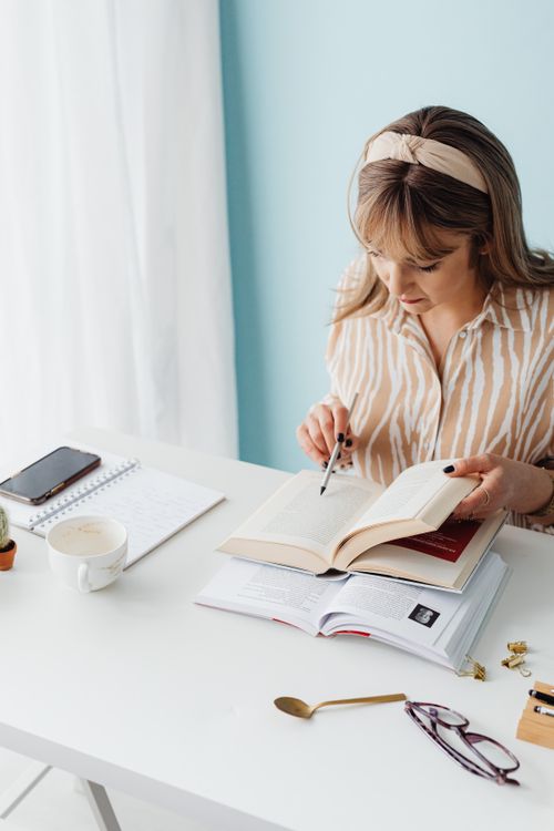 Free A woman reads a book at a desk with a notebook and coffee in a bright room. Stock Photo