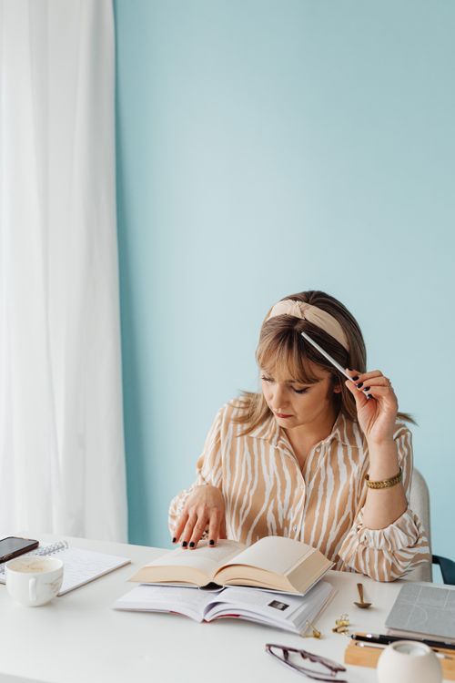 Free Woman in casual attire sitting at a desk, studying with books, in a calm and bright indoor setting. Stock Photo