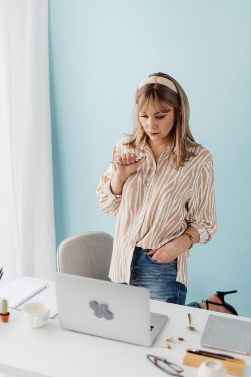 Free Focused woman standing at desk using laptop for work in modern office. Stock Photo