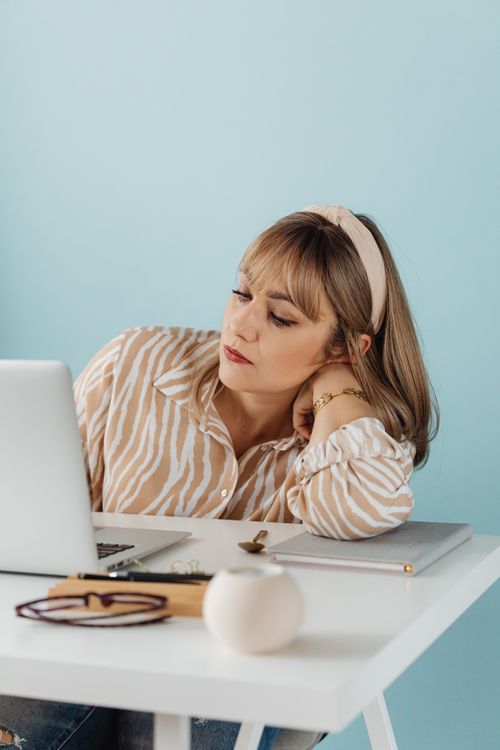 Free Woman in casual attire working on a laptop at a white desk, light blue background, indoors. Stock Photo