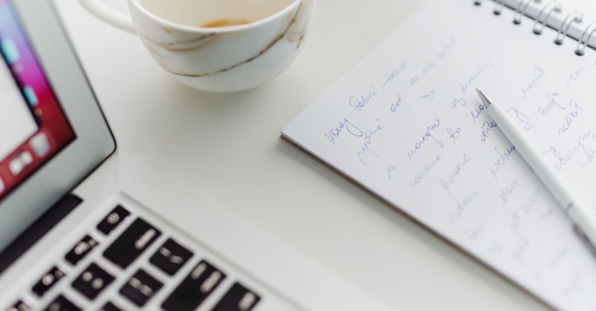A notebook with handwritten recipe notes, a cup of coffee, and a laptop showing a food blog