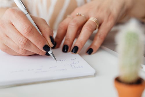 Free Person with Black Nail Polish Writing on White Paper Stock Photo