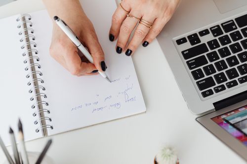 Free Hands writing on notepad beside a laptop on a white desk, indoors. Stock Photo