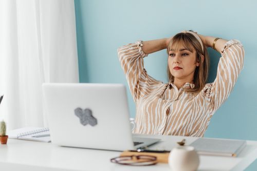 Free A woman resting at a desk, leaning back with hands behind head, in a home office setting. Stock Photo