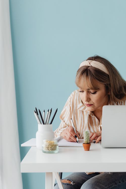Free Caucasian woman writing at desk with laptop and pencils, focused on work. Stock Photo
