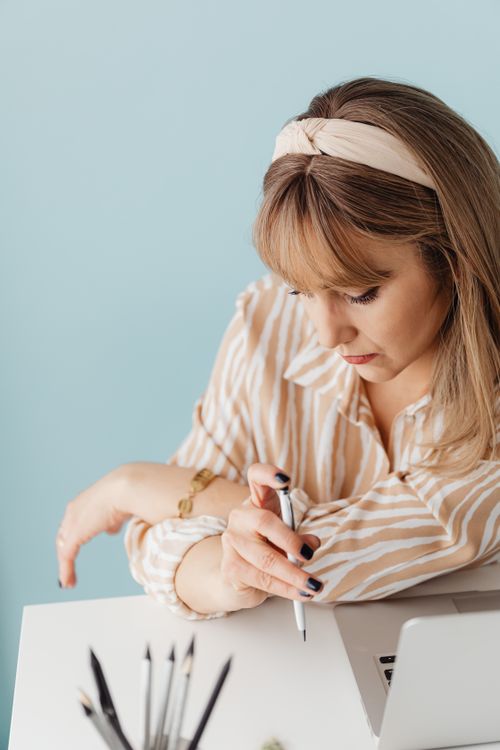 Free Caucasian woman in striped shirt writing with a pen next to a laptop. Stock Photo