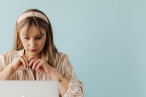 Free A thoughtful woman with a headband works intently on a laptop against a blue background. Stock Photo
