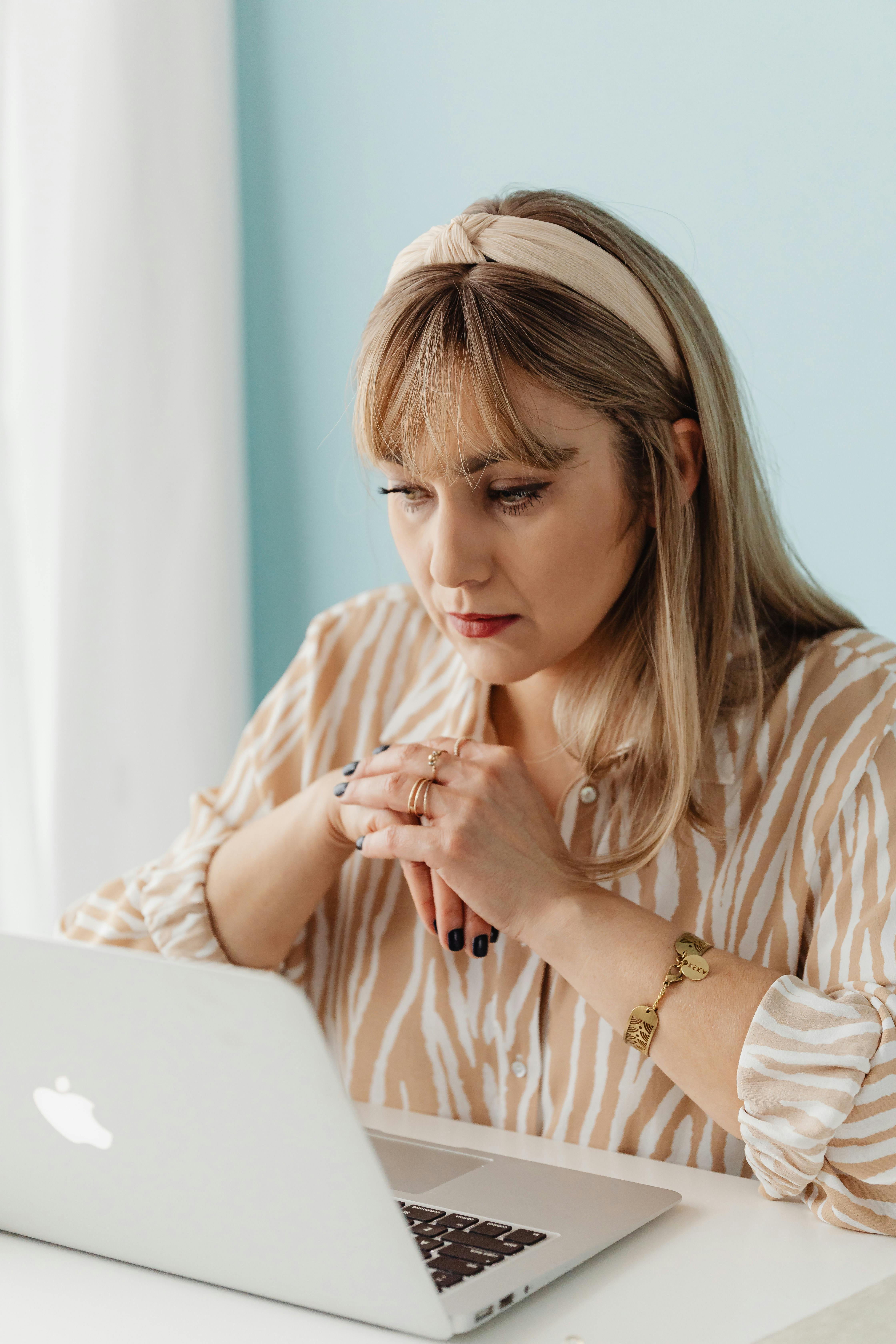 Woman in a striped blouse and headband concentrating on work at a laptop in well-lit indoor space.