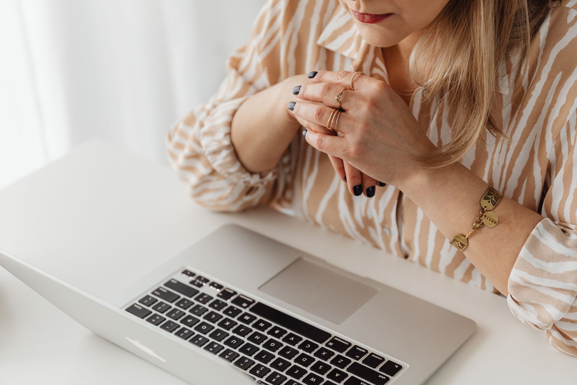 A woman wearing jewelry works remotely on her laptop, depicting modern workplace style.