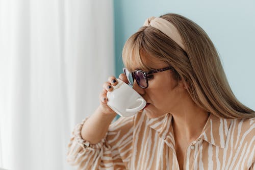 Woman in a Beige Pattern Blouse Drinking Coffee from a White Cup
